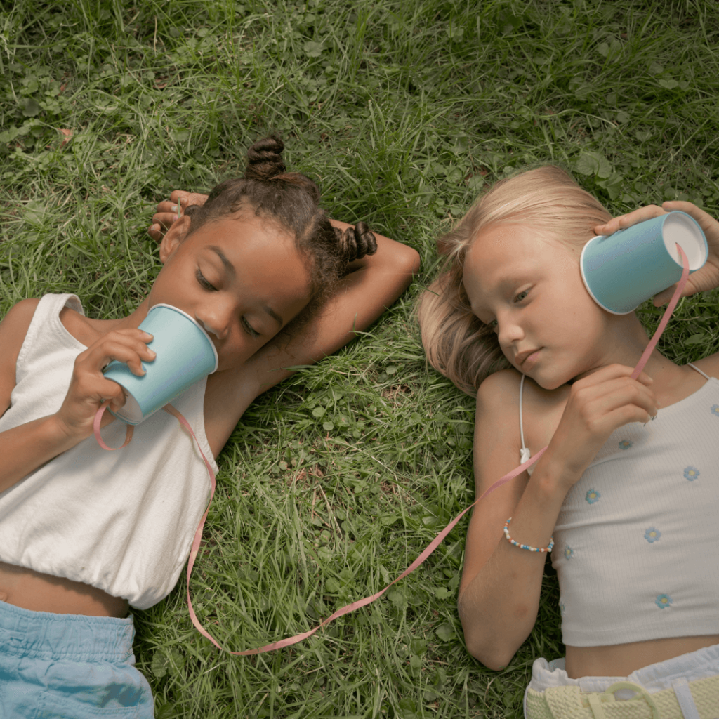 Girls laying in the grass chatting through paper cup phones