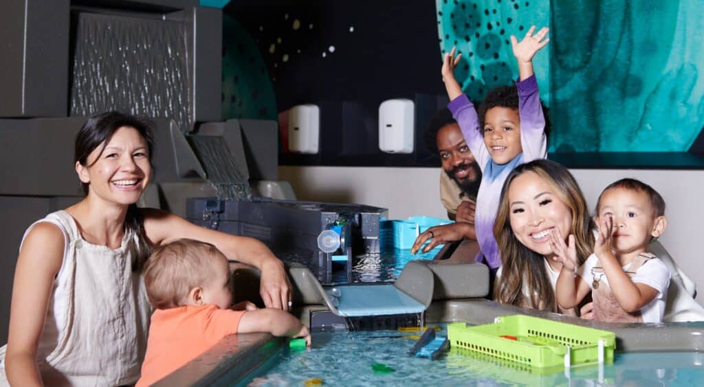 Group of parents and toddlers playing with water in the science playground at OMSI