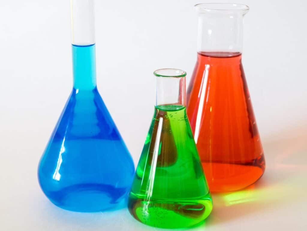 Three chemistry narrow neck flasks filled with colorful liquid.
