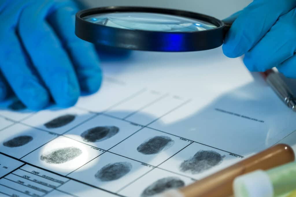 lab tech wearing plastic gloves holding a microscope to examine various fingerprints