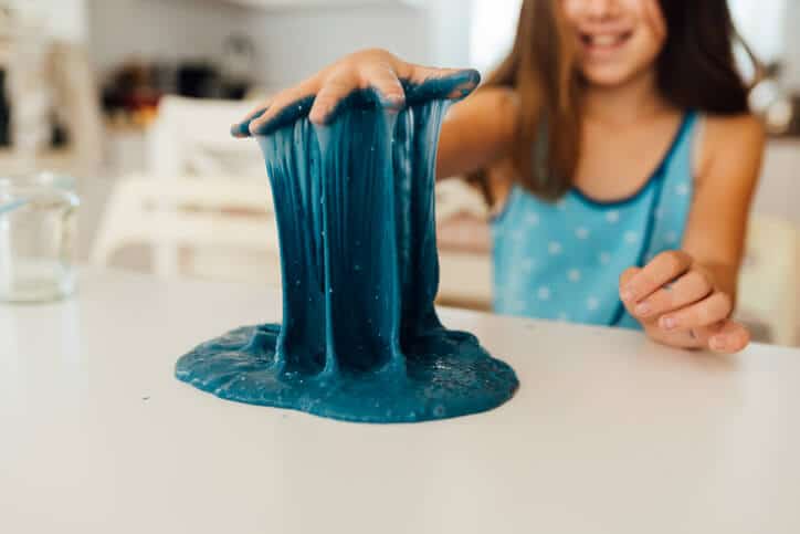 Girl pulling blue slime up from a table