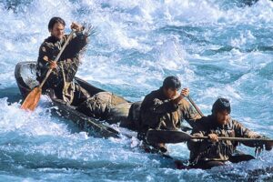 Three individuals in a canoe navigating river rapids.