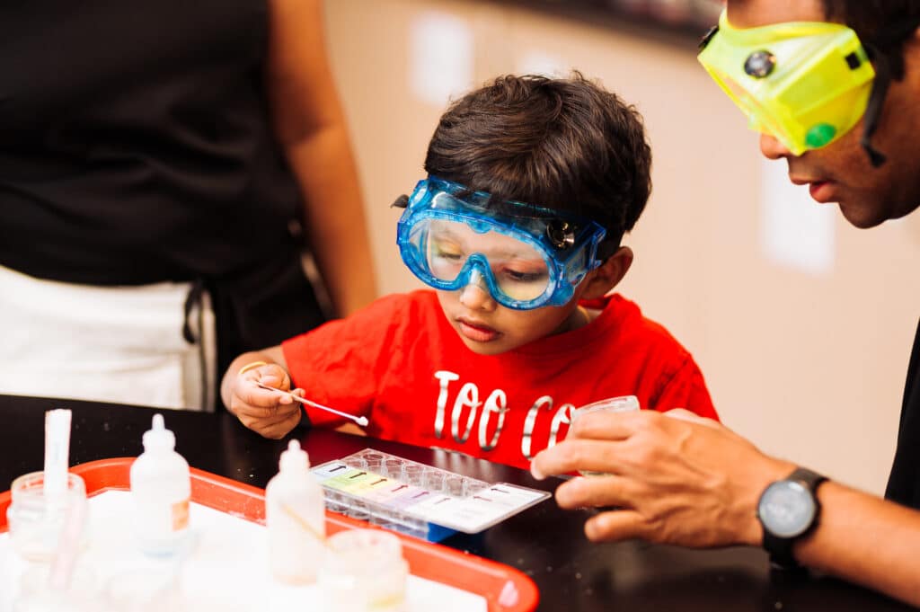 A young child wears goggles as they use a dropper to complete a chemistry experiment.