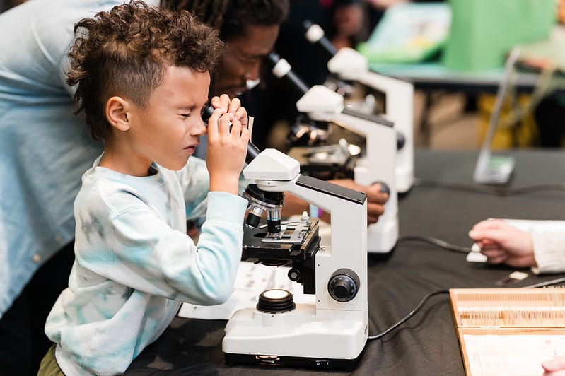 A young boy looks through the eyepiece of a microscope.