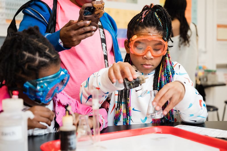 Two girls practice chemistry in a lab.