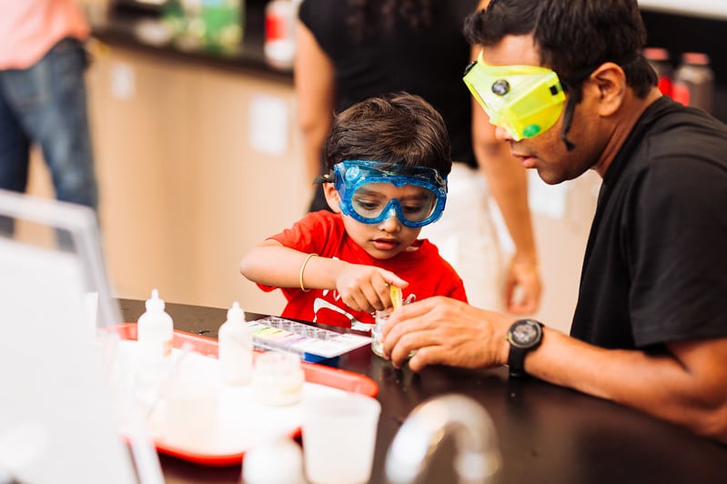 Father and son wearing science goggles doing an experiment in the chemistry lab at OMSI
