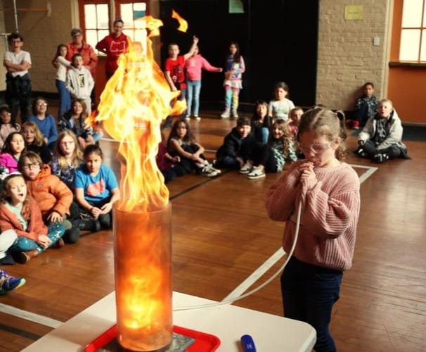 Roosevelt and Conger elementary school students take part in an assembly by OMSI where one child breathes air into a tube to stoke a fire.