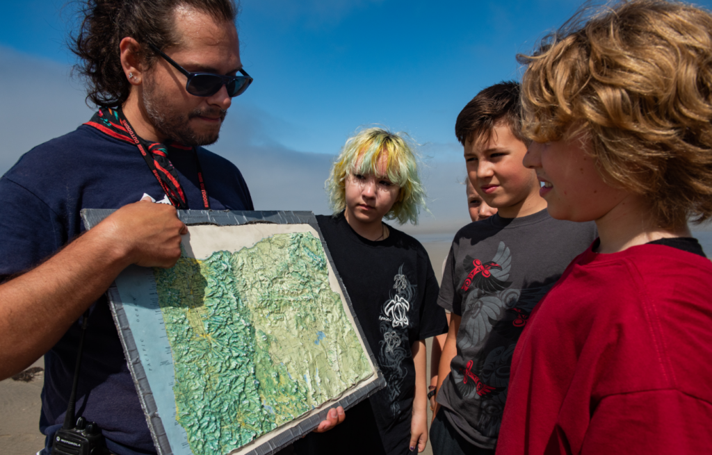 Photo of counselor showing campers an interactive map on the beach at Camp Gray