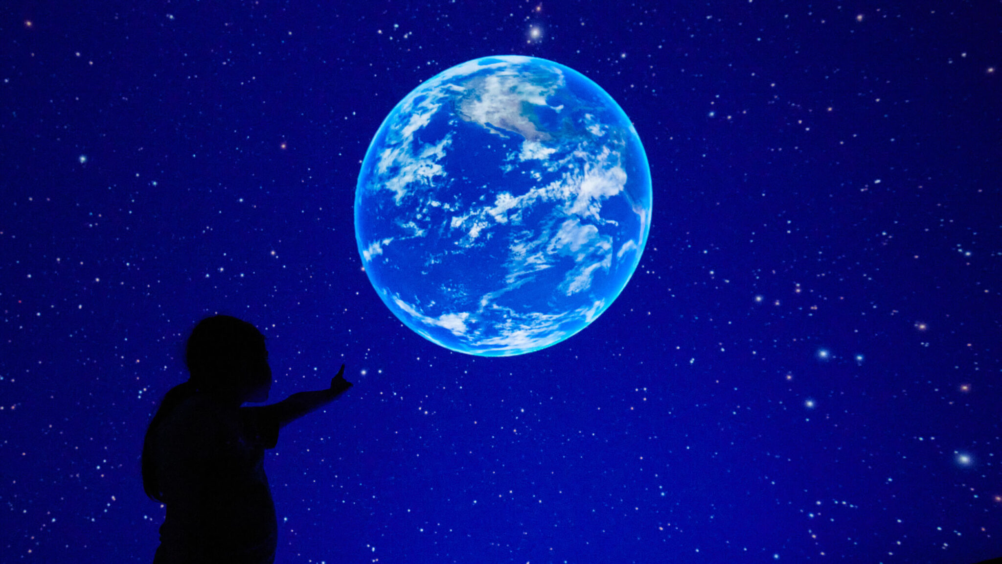 Silhouette of a child pointing at a picture of the earth in space