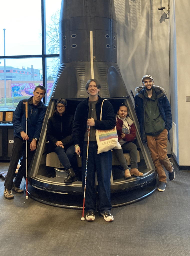 Five students from the Washington State School for the Blind pose by OMSI's space capsule during their visit to test Aira at the museum.