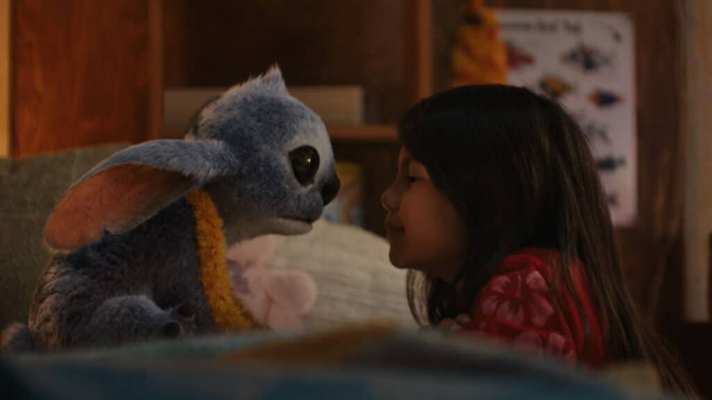 Blue furry alien and young girl face to face sitting on a bed
