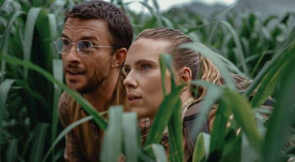 Blonde woman and brunette man with glasses crouching in tall grass