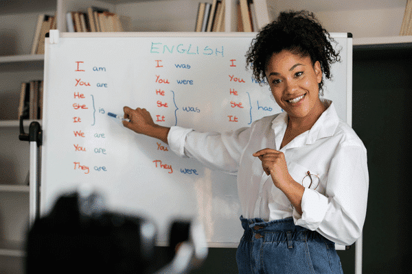 A woman teaching English grammar on a white board to a camera