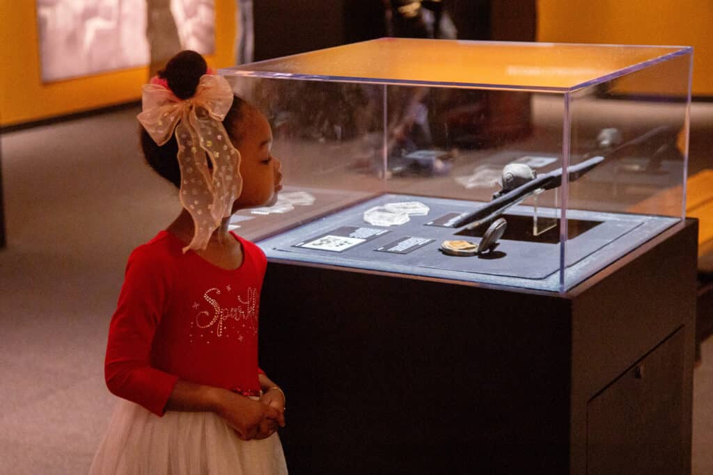 A young girl looks at an artifact from the Titanic wreck site that is under glass. The artifact is a small powder case that has been recovered from the ocean floor by the RMS Titanic.
