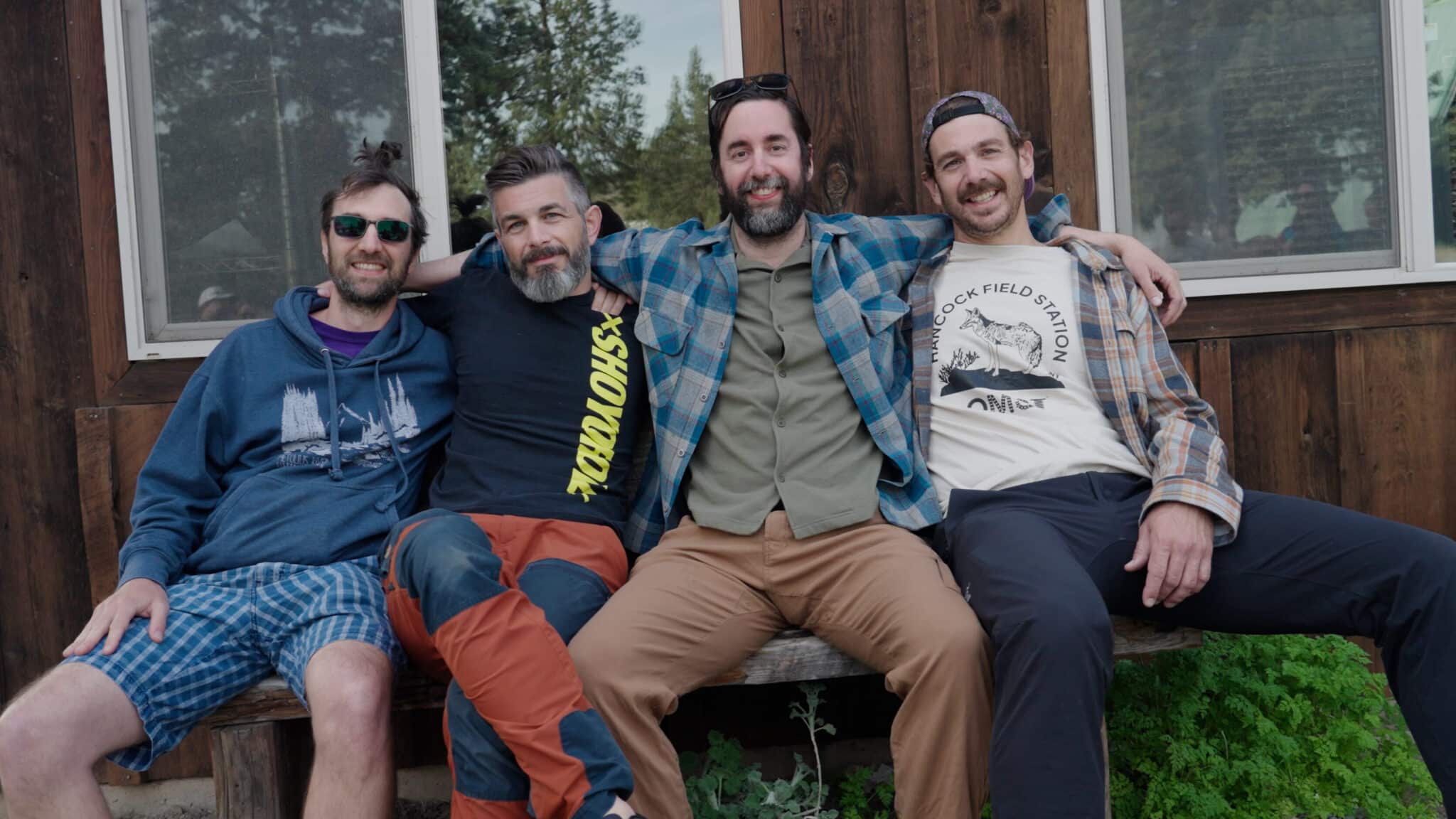 Four men sit on a bench at Camp Hancock with their arms wrapped around each other