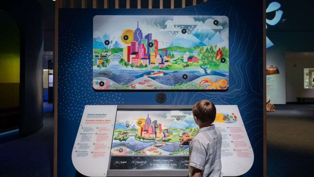 A young boy plays with the tactile mural in the Natural Sciences Hall. The mural uses bright colors and various layers to depict a cityscape, mountain range, river, farm, and forest.