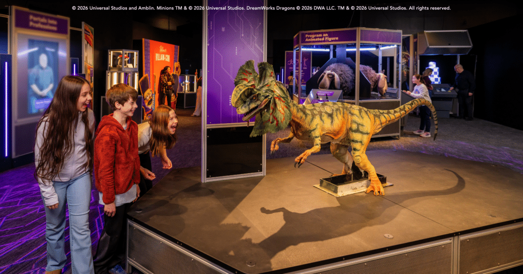 An image of three children at Universal Theme Parks: The Exhibition. They are looking at a life sized replica of a dinosaur from the film Jurassic World.
